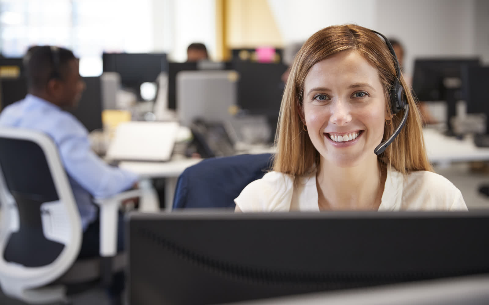 A support specialist wearing a headset at her desk in a busy open plan office.