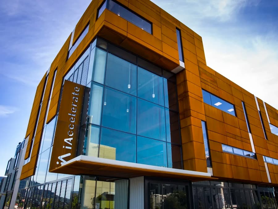 The iAccelerate building at the University of Wollongong Innovation Campus, its weathered steel and glass facade seen from below against a clear sky.